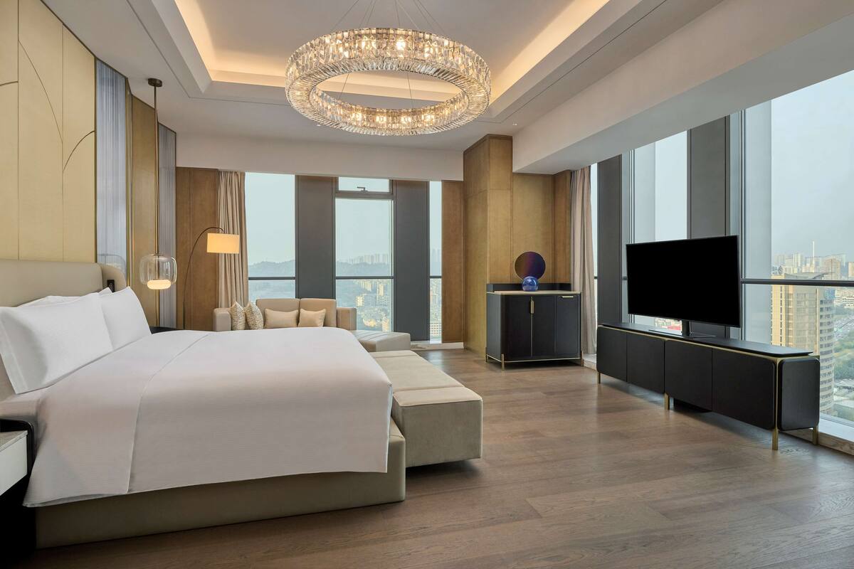 Une chambre d’hôtel moderne dotée d’un grand lit, d’une télévision, d’un canapé et offrant une vue sur la ville.