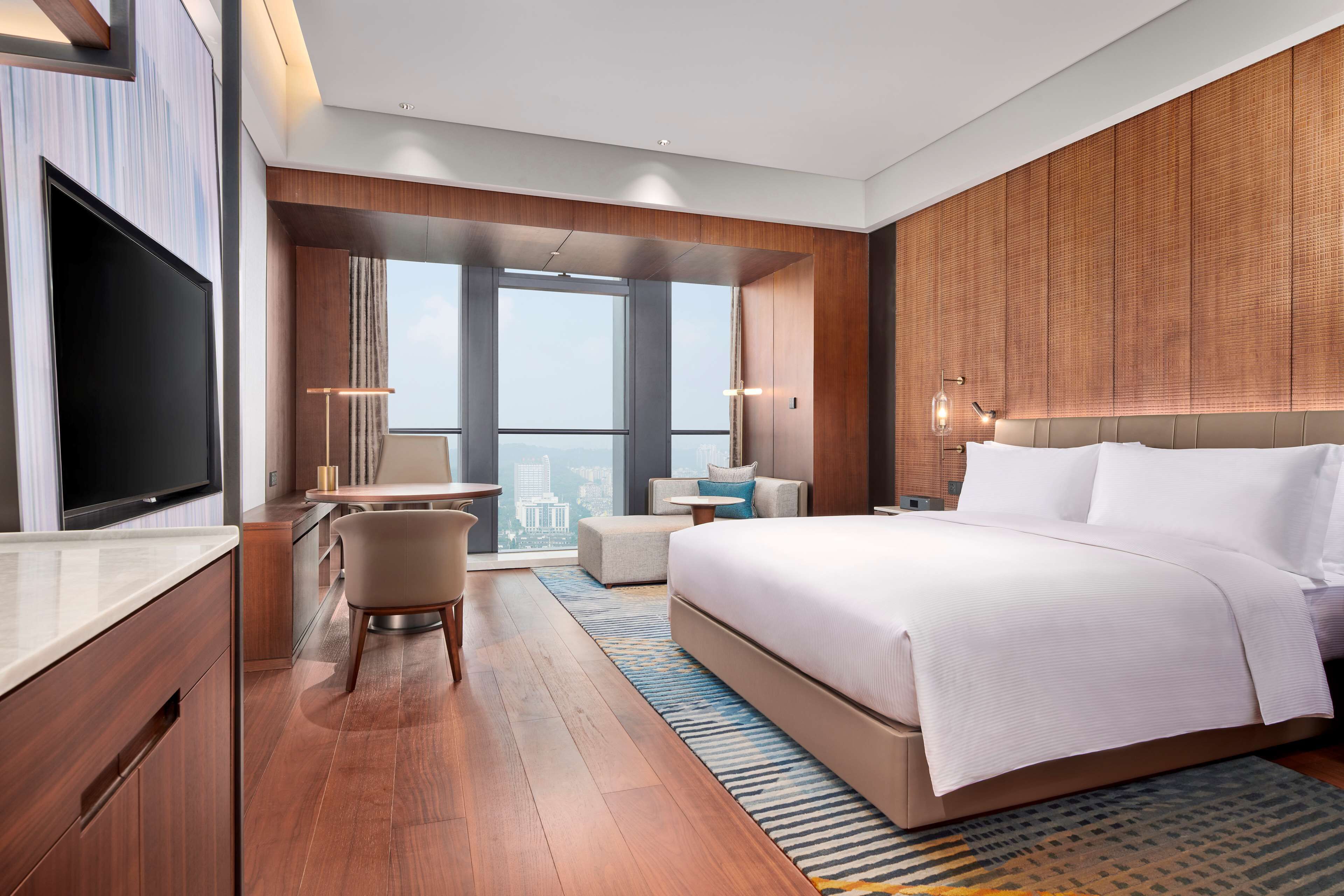 A modern hotel room with a large bed, a desk, a chair, and a television.