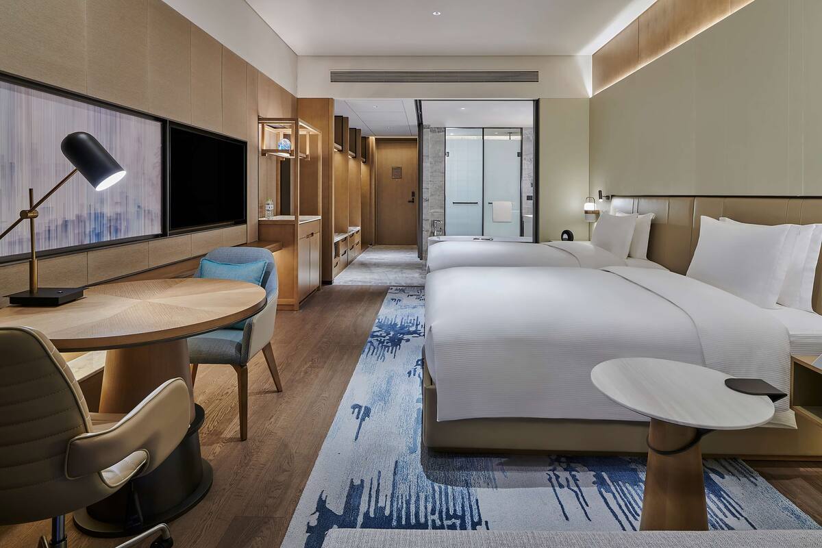 Une chambre d’hôtel moderne dotée d’un grand lit, d’un bureau avec une chaise, d’une petite table et d’une grande fenêtre.