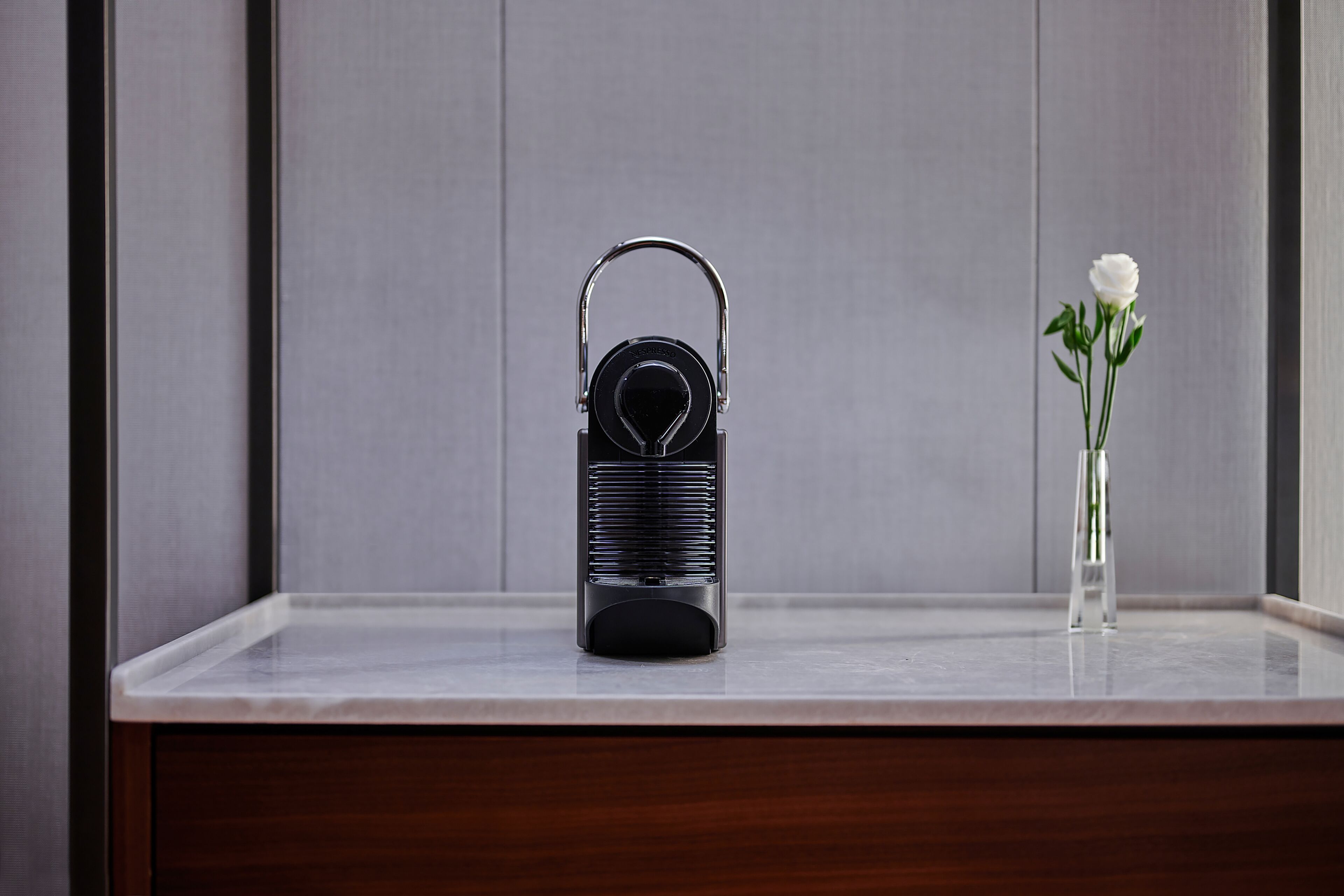 A black portable speaker on a marble surface with a white flower in a clear vase.