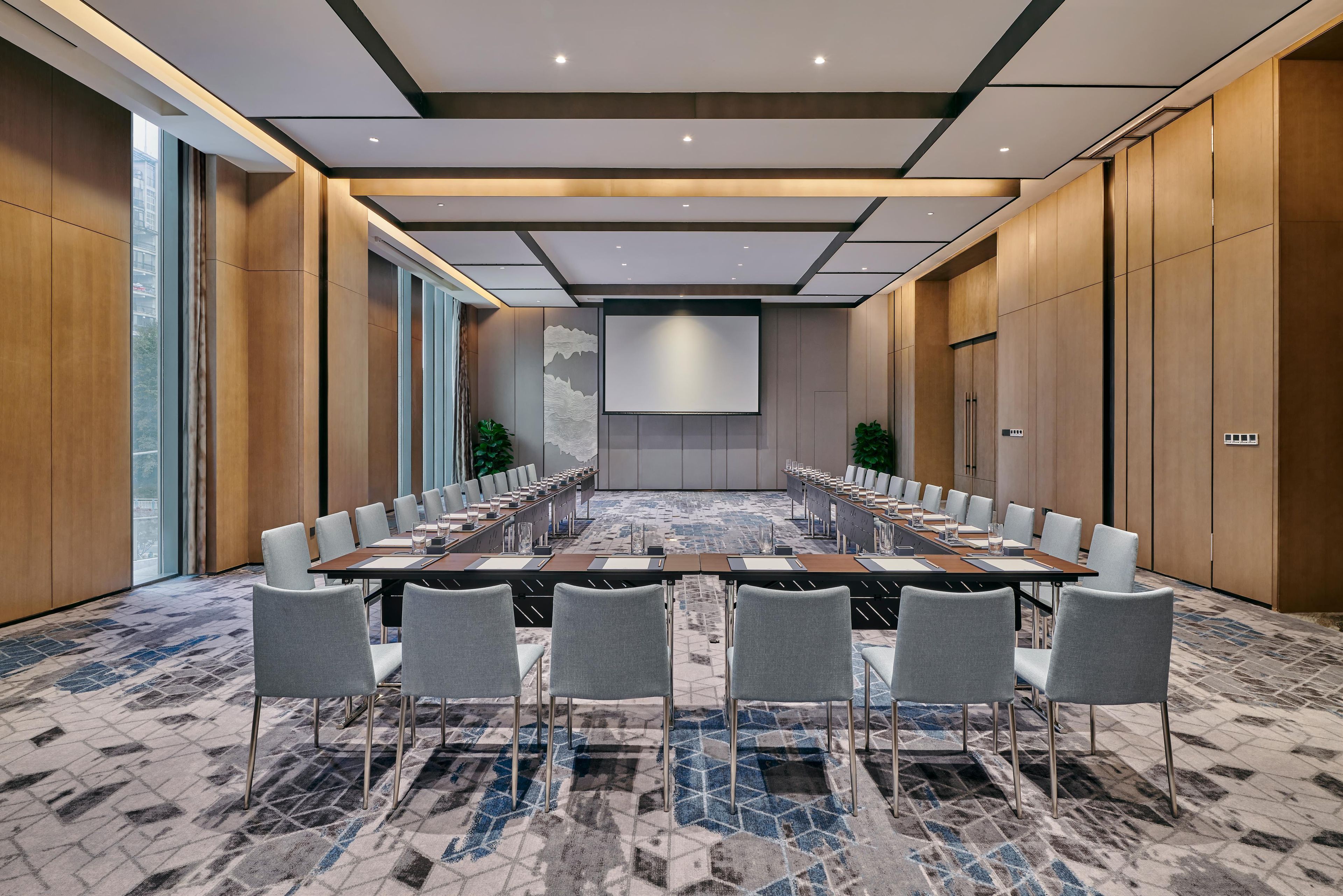 Une salle de conférence avec une longue table, de nombreuses chaises, un grand écran et une moquette à motifs.