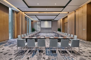 Una sala conferenze con un lungo tavolo, diverse sedie, un grande schermo e un tappeto decorato.