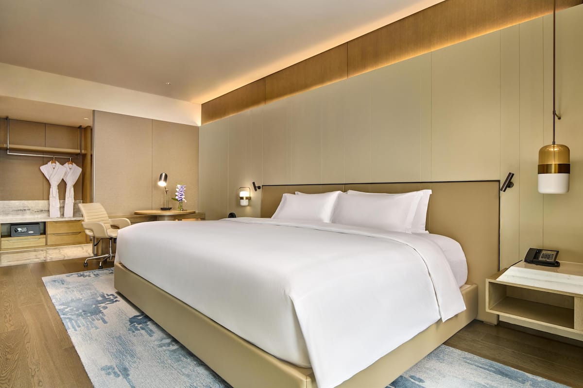 Une chambre d’hôtel moderne dotée d’un grand lit, de tables de chevet, d’un bureau avec une chaise et d’une coiffeuse avec un miroir et un porte-serviettes.