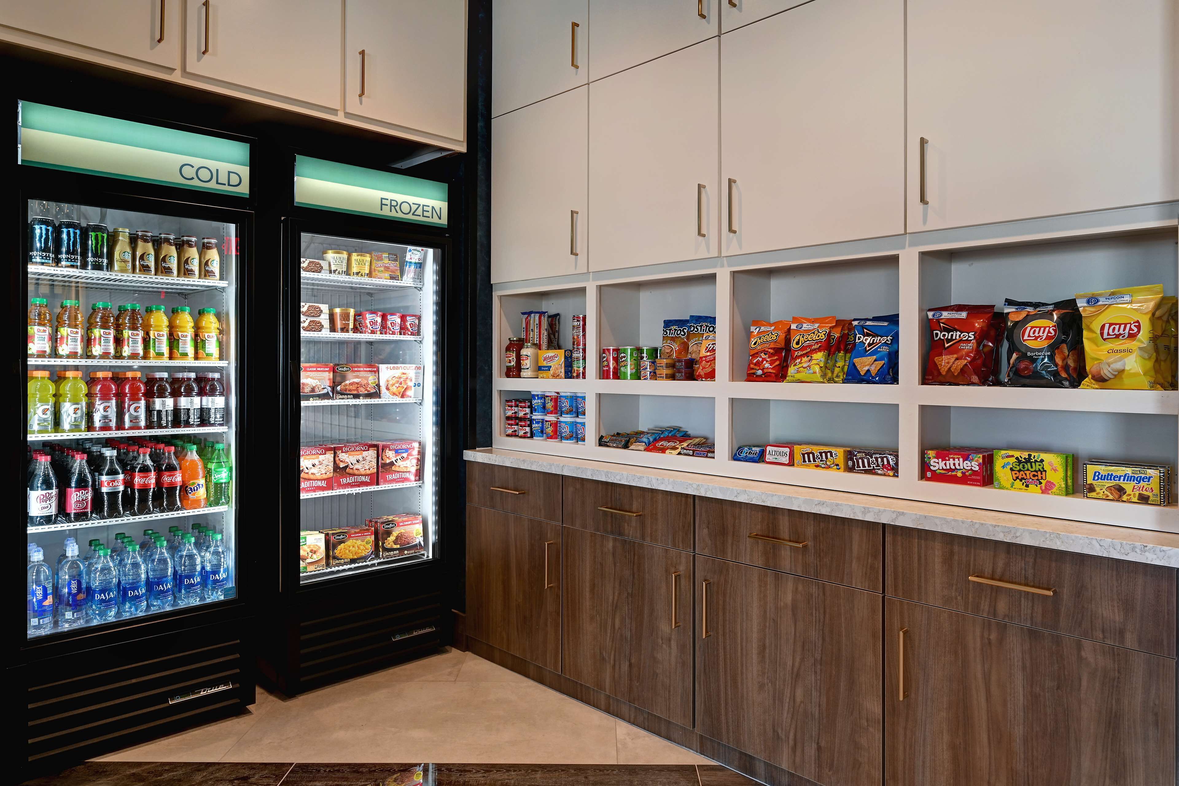 A snack and beverage area with refrigerated and frozen sections, shelves stocked with chips, cookies, and other snacks.