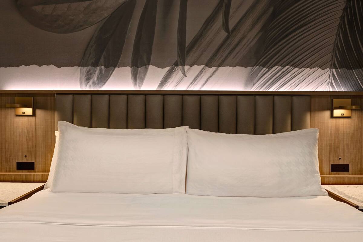 A neatly made bed with two pillows, a headboard with vertical slats, and wall-mounted lighting on either side.