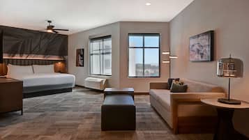 A modern hotel room with a bed, a sofa, a coffee table, and a large window offering a city view.