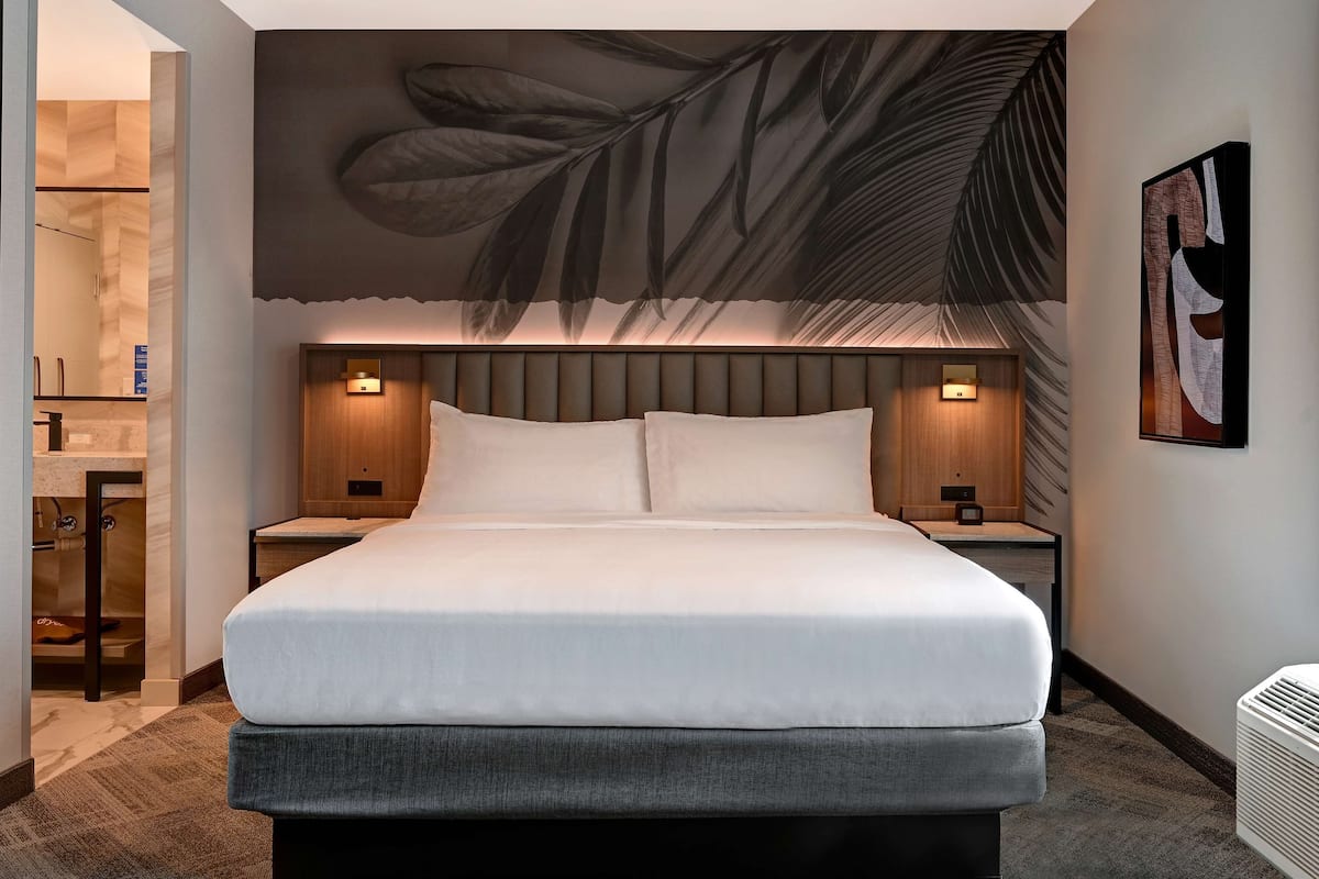 A modern hotel room with a large bed, two bedside tables, and a wall-mounted artwork.