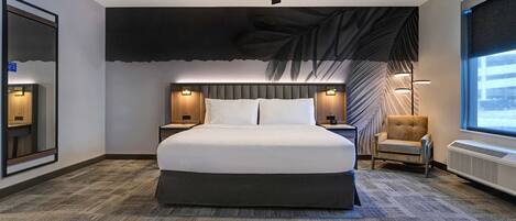 A hotel room with a large bed, a ceiling fan, a wall-mounted TV, a chair, and a window with a view.