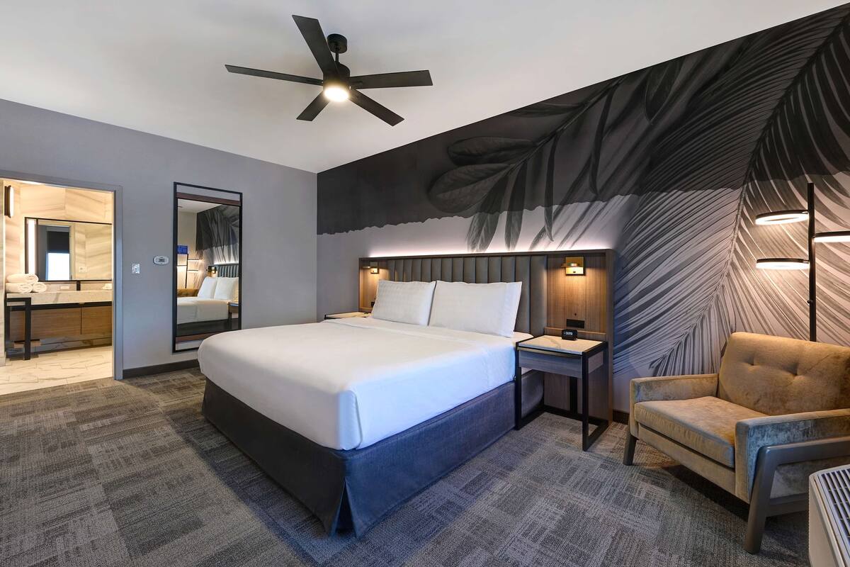 A modern hotel room with a large bed, a ceiling fan, a sofa, and a mirror.