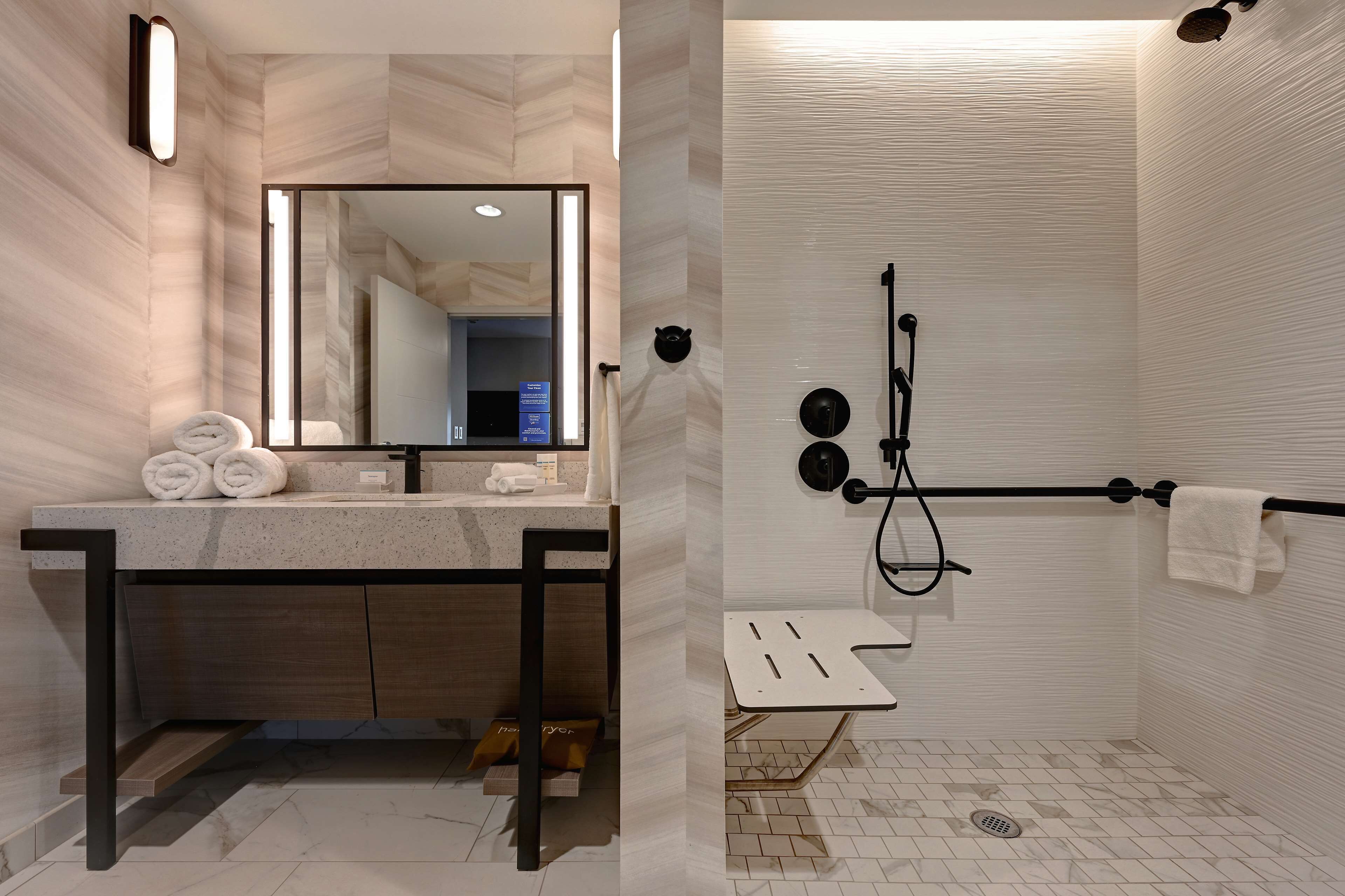 Un baño moderno con un espejo grande, un lavamanos con toallero y una zona de ducha con barra para toallas.