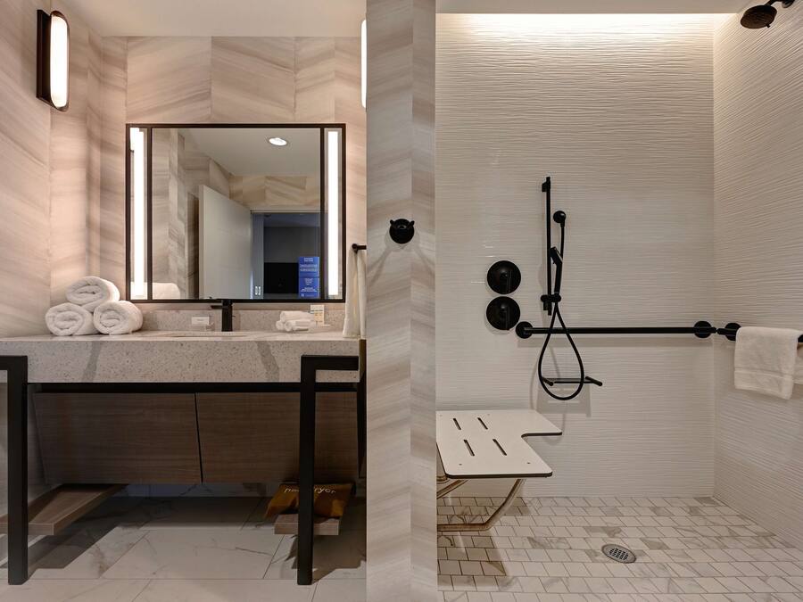 Un baño moderno con un espejo grande, un lavamanos con toallero y una zona de ducha con barra para toallas.