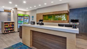 A hotel reception area with a counter, a minibar, a vending machine, and a self-service kiosk.