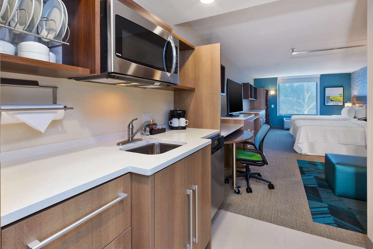 Une chambre d’hôtel moderne équipée d’une kitchenette, d’un lit, d’un bureau et d’une grande fenêtre.