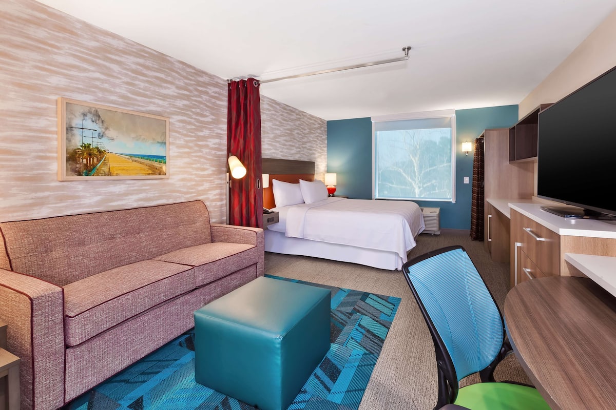Une chambre d’hôtel avec un lit, un canapé, un bureau, une télévision et un tableau au mur.
