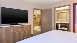Une chambre d’hôtel dotée d’une grande télévision à écran plat, d’un lit, d’une coiffeuse avec un miroir et d’un dressing.