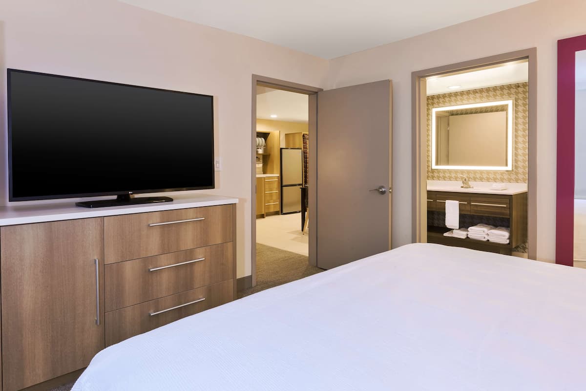 Une chambre d’hôtel dotée d’une grande télévision à écran plat, d’un lit, d’une coiffeuse avec un miroir et d’un dressing.