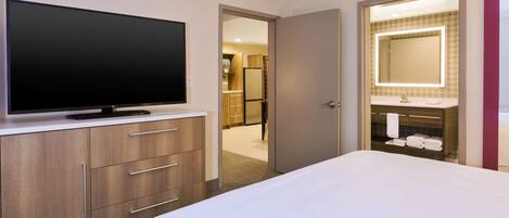 Habitación de hotel con una televisión de pantalla plana grande, una cama, una tocador con espejo y un vestidor.