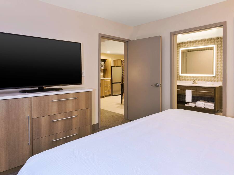 A hotel room with a large flat-screen TV, a bed, a vanity with a mirror, and a walk-in closet.