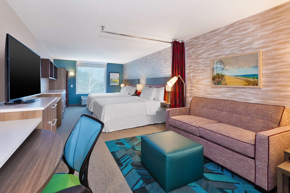 Une chambre d’hôtel avec un lit, un canapé, un bureau avec un ordinateur, une télévision et un tableau au mur.