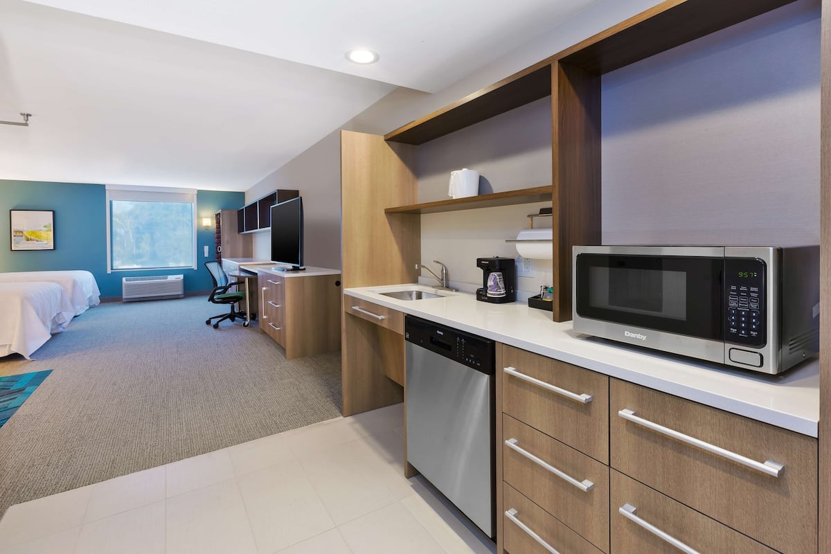 Une chambre d’hôtel moderne équipée d’une kitchenette, d’un lit, d’un bureau et d’une grande fenêtre.