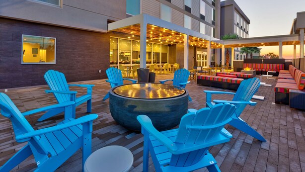 Un espace extérieur moderne, aménagé avec des chaises Adirondack bleues, une table ronde et un coin bar illuminé de guirlandes lumineuses.