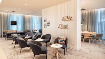 A modern hotel lobby with a seating area, a dining table, and a TV mounted on the wall.