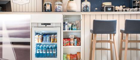 A kitchenette with a refrigerator, a pantry with snacks, and two bar stools.