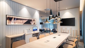 Uma sala de conferências moderna com uma mesa comprida, várias cadeiras, uma televisão grande e iluminação pendente.