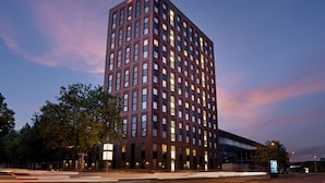 Um hotel alto e moderno, com um letreiro chamativo "Hampton" no topo, com uma grade de janelas e telhado plano.