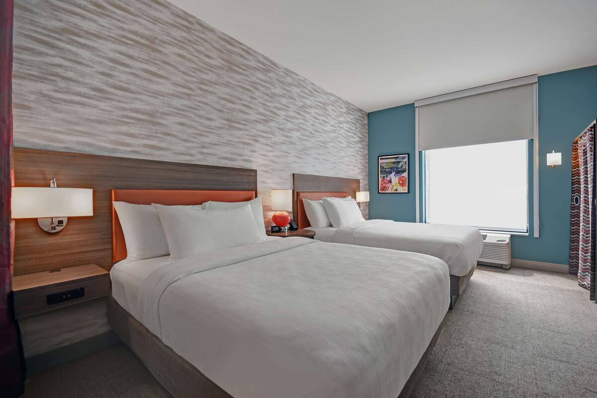 A hotel room with two beds, a large window, and a textured wall.
