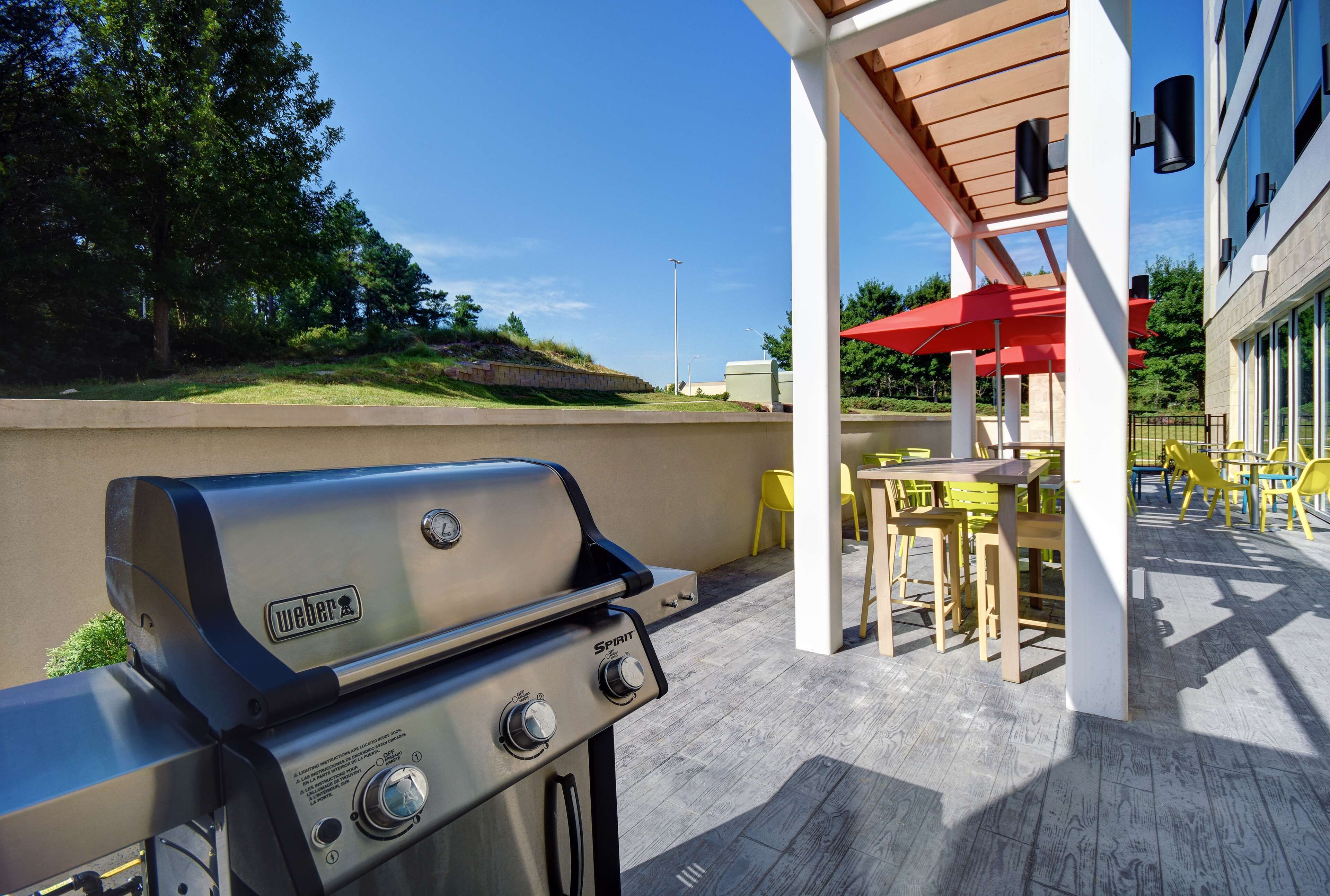 Eine Terrassengruppe im Freien mit einem Weber Spirit Grill, gelben Stühlen und einem roten Sonnenschirm.