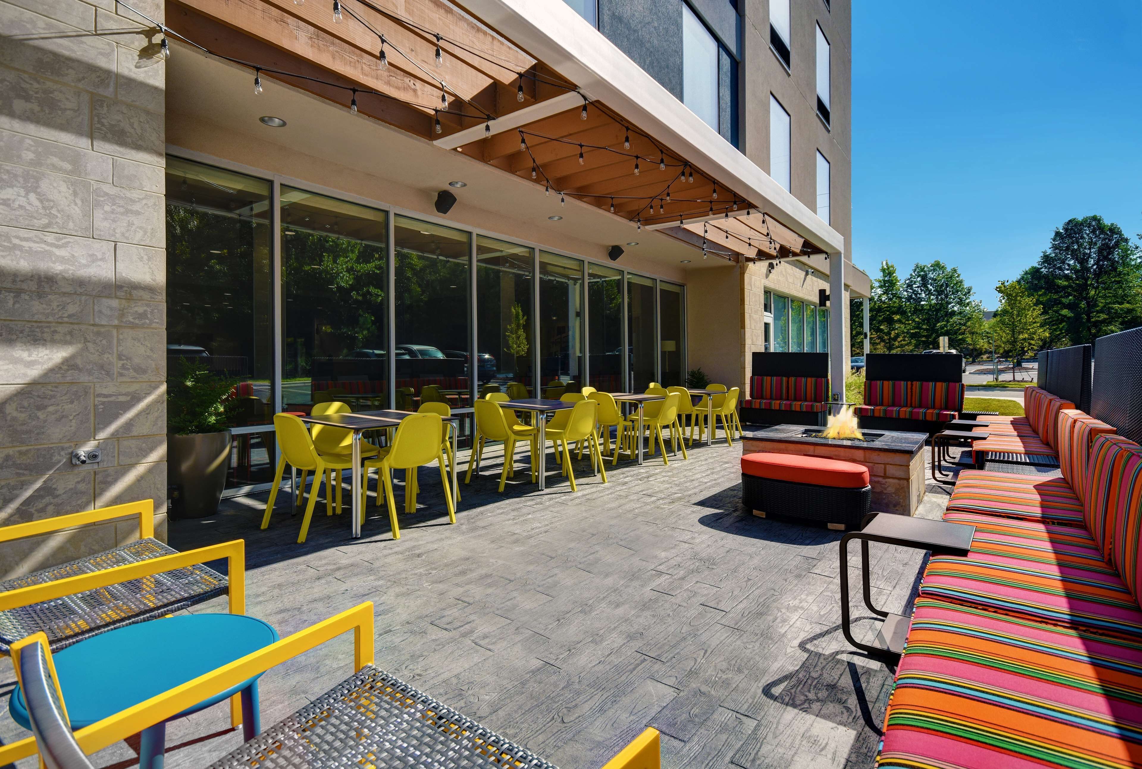 An outdoor seating area with yellow chairs and tables, a fire pit, and a colorful striped sofa.