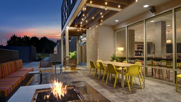 An outdoor patio area with a fire pit, yellow chairs, and a dining table. - Home2 Suites by Hilton Raleigh North I-540 (Raleigh)