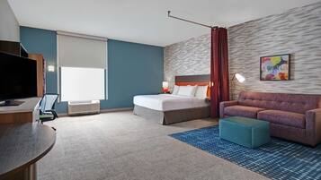 A hotel room with a bed, a sofa, a desk with a TV, and a large window with blinds.