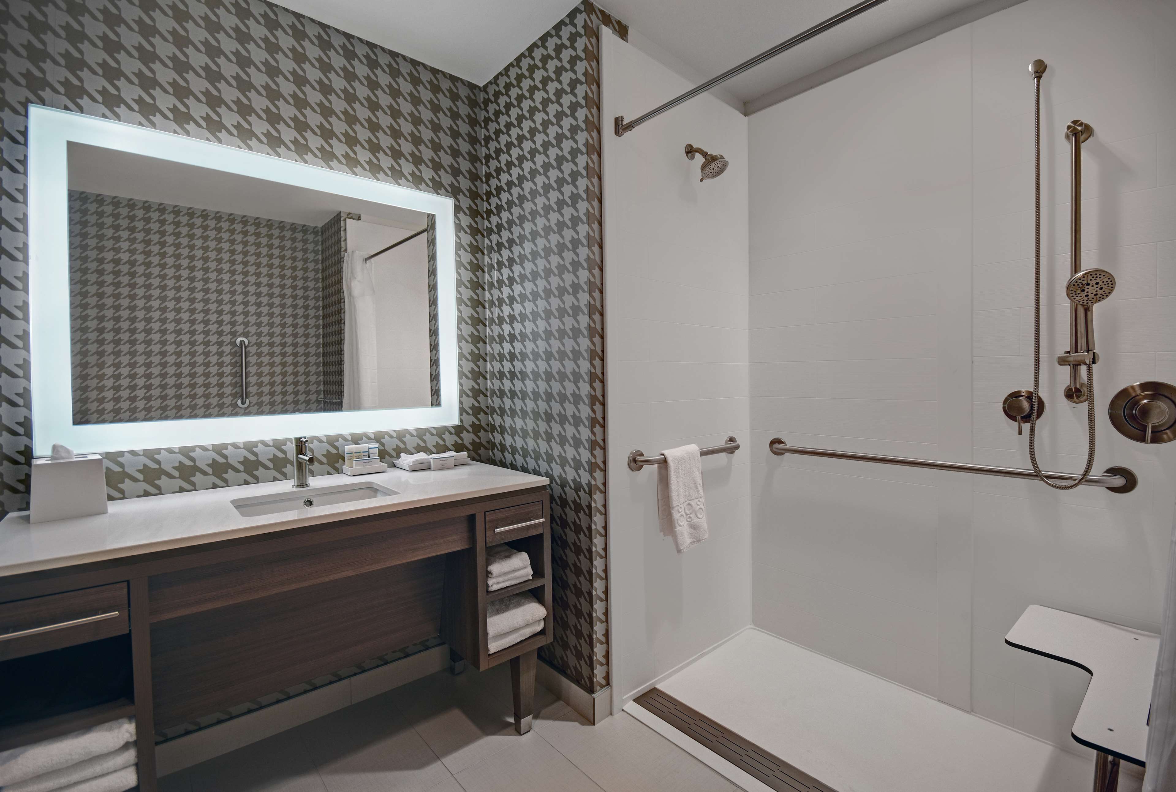 A modern bathroom with a large mirror, two sinks, a shower with a handheld showerhead, and a towel rack.