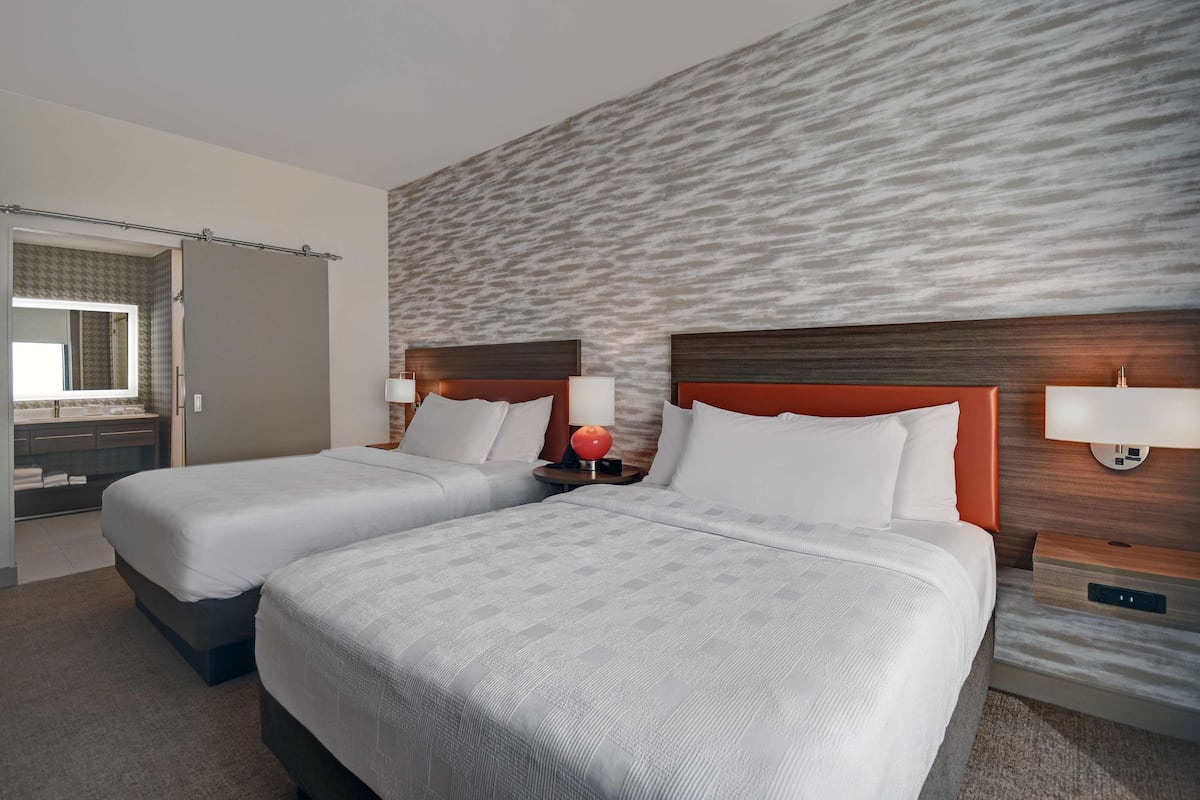A hotel room with two beds, a bathroom, and a large textured wall.