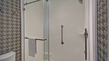 A glass-enclosed shower with a handheld showerhead, a towel rack, and a toilet visible in the adjacent bathroom.