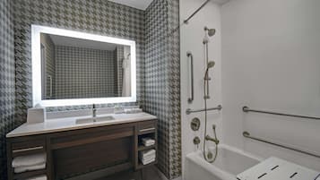 A modern bathroom with a large mirror, a bathtub, and a shower with grab bars.