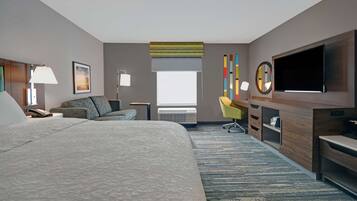 Hotelkamer met een groot bed, een bureau, een flatscreen televisie, een stoel, een lamp en een raam met zonwering.