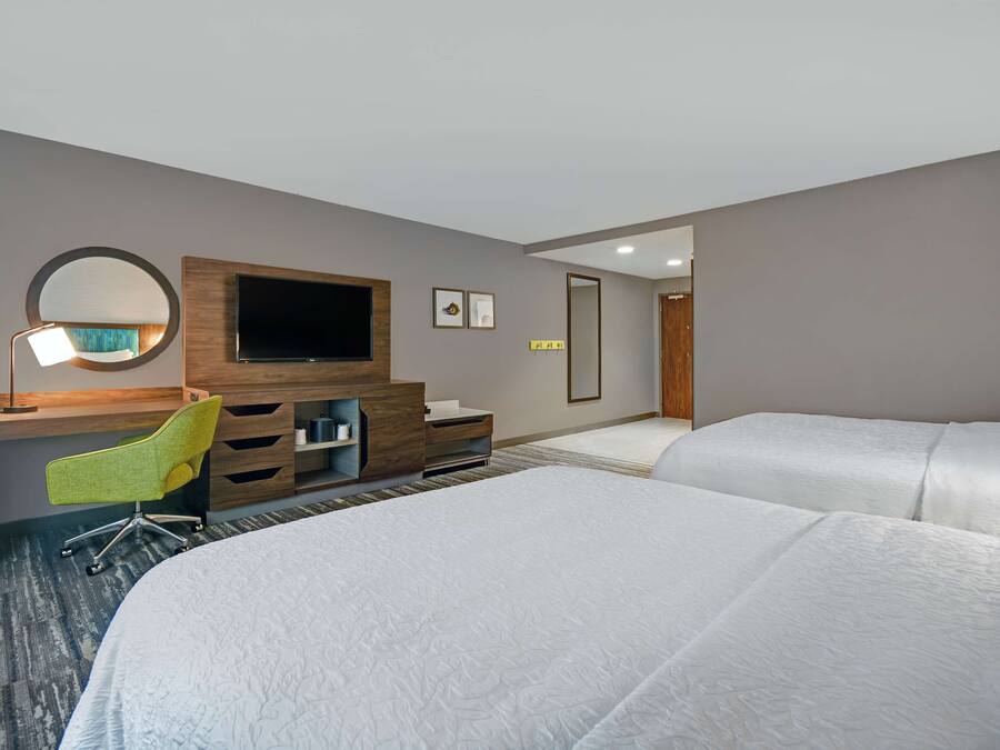 A hotel room with a large bed, a desk with a chair, a television, and a mirror.