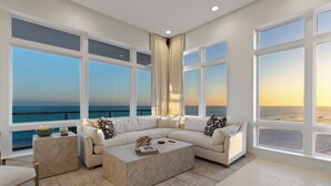 Un salon spacieux avec une grande fenêtre donnant sur la mer, un canapé d’angle beige, une table basse et un tapis à motifs.