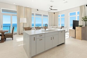 A modern kitchen with a large island, a dining area with a view, and a living space with a sofa and TV.