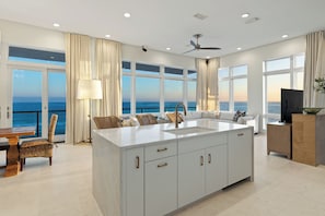 Una cocina moderna con una isla grande, un comedor con vistas al mar y una sala de estar con sofá y televisor.