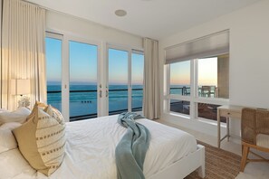 A bedroom with a bed, a desk, and a view of the ocean.