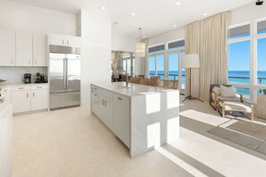 A modern kitchen with a large island, white cabinetry, and a view of the ocean.