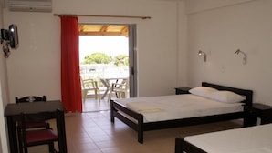 Ein Schlafzimmer mit einem Bett, einem Schreibtisch und einem Stuhl. Eine Tür führt zu einem Außenbereich mit Tisch und Stühlen.