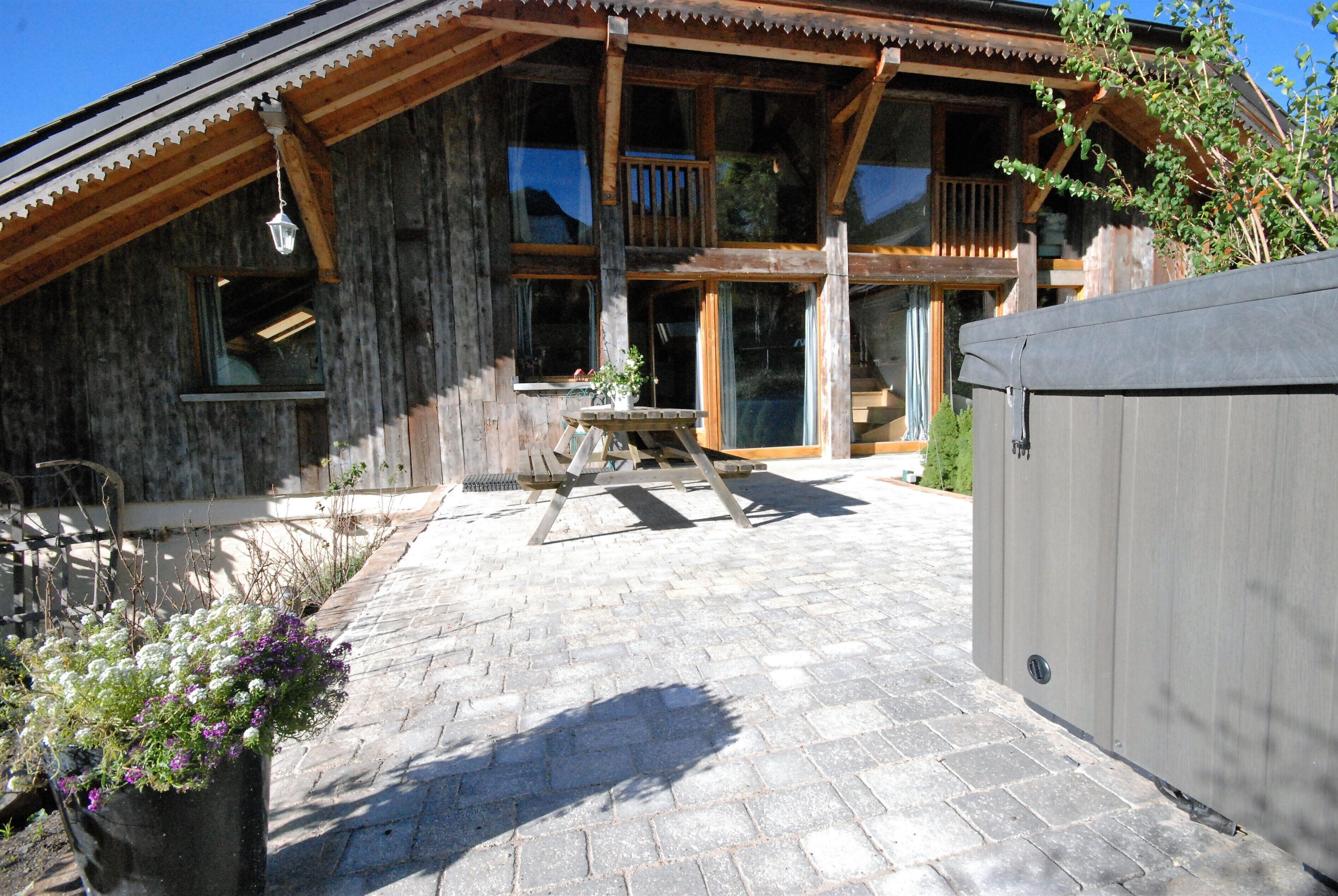 A wooden chalet with a balcony, stone-paved patio, and a large window overlooking the interior.