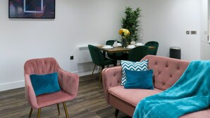 Ein modernes Wohnzimmer mit einem rosafarbenen Sofa, einem rosafarbenen Sessel und einem Essbereich mit Tisch für zwei Personen.