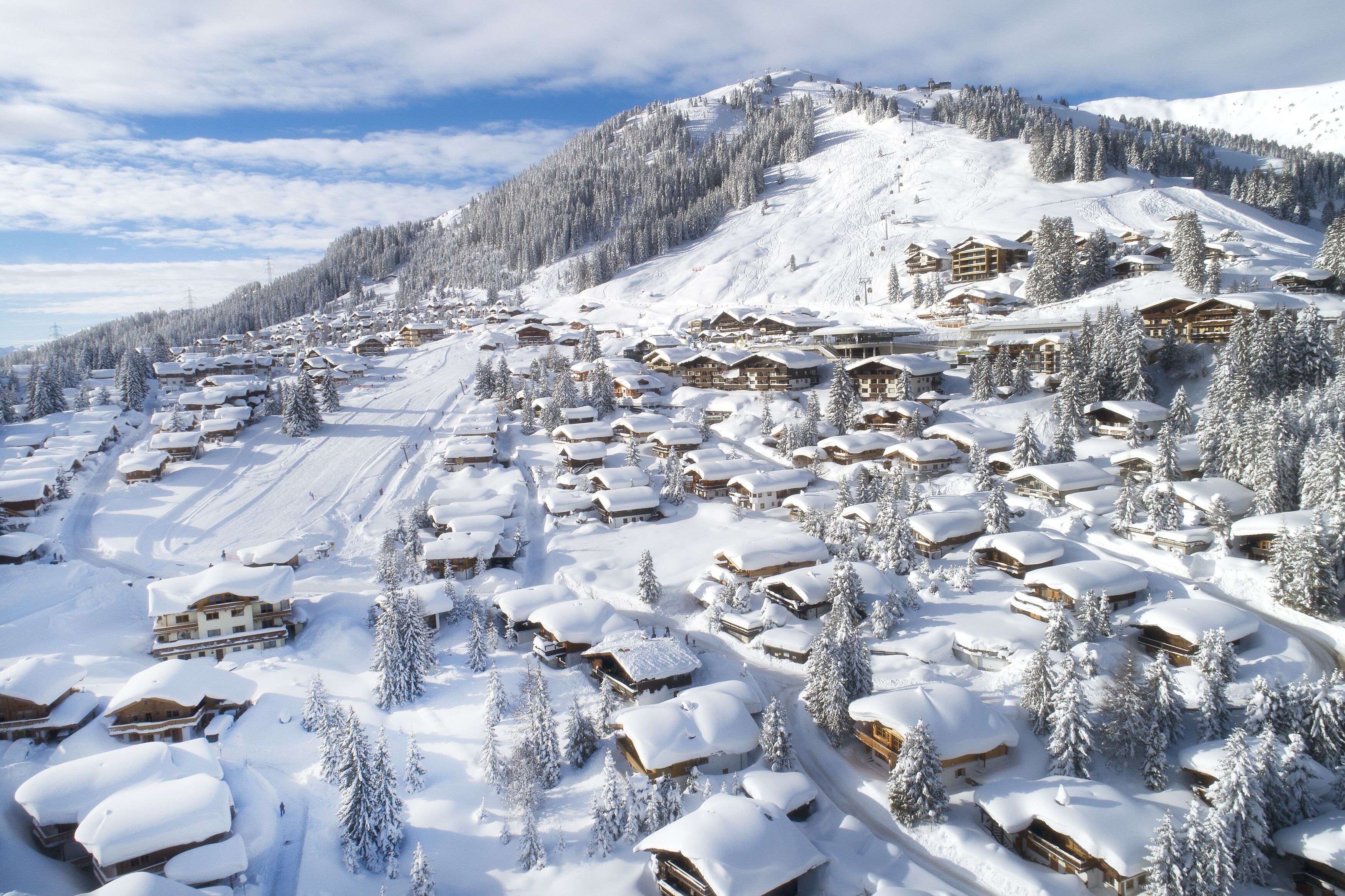 A snow-covered village with wooden chalets and a ski slope.