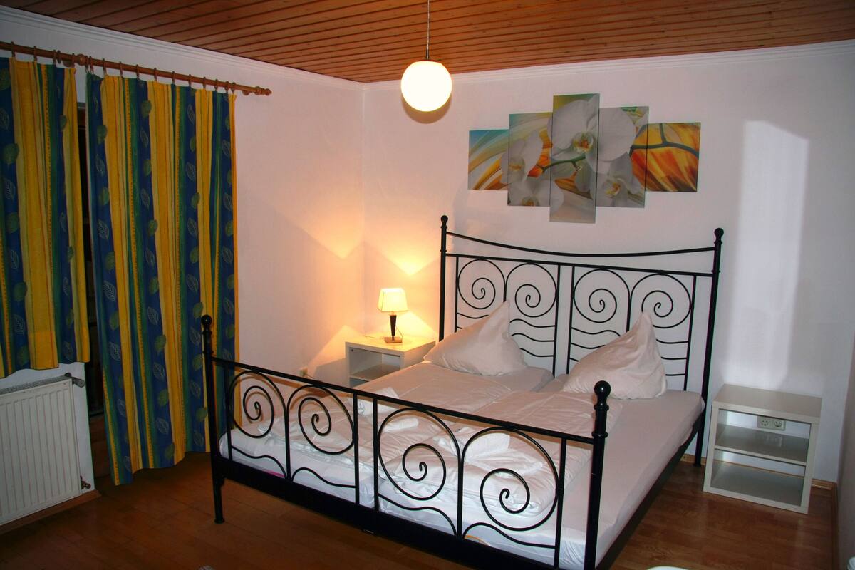 Une chambre à coucher avec un lit, une table de chevet, une lampe et une œuvre d’art accrochée au mur.